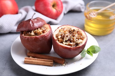 Tasty baked apples with nuts, honey, cinnamon sticks and mint on gray table, closeup