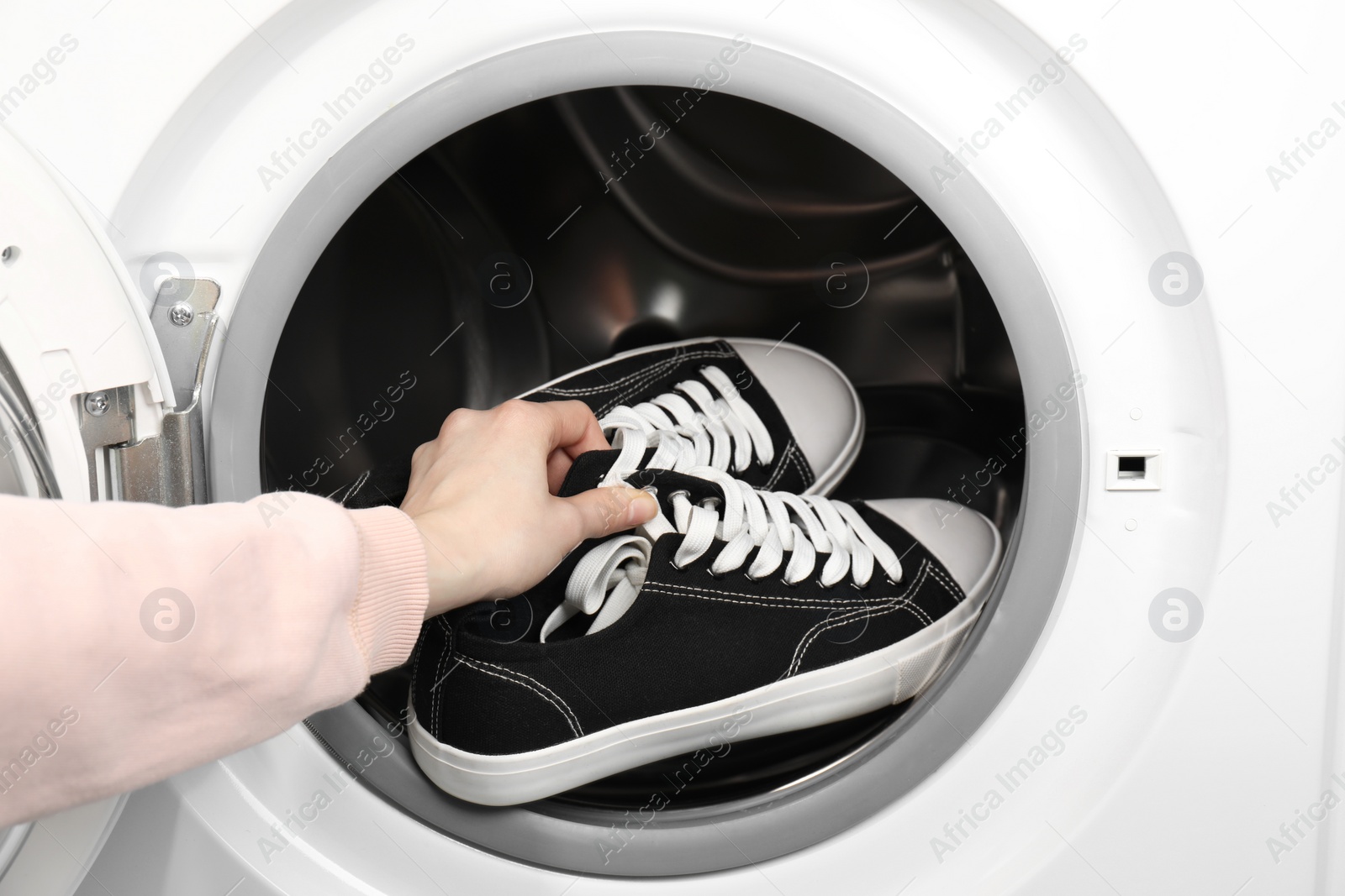 Photo of Woman putting stylish sneakers into washing machine, closeup