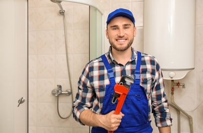 Professional plumber in uniform with pipe wrench indoors