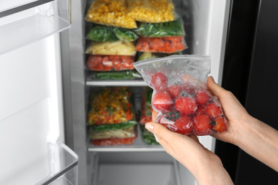 Photo of Woman holding plastic bag with frozen tomatoes near open refrigerator, closeup