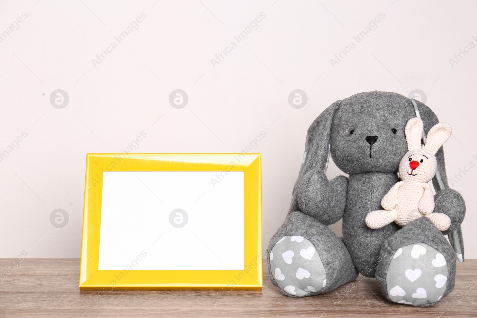 Photo of Photo frame and adorable toy bunnies on table against light background, space for text. Child room elements