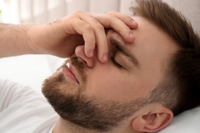Photo of Young man suffering from migraine in bed, closeup
