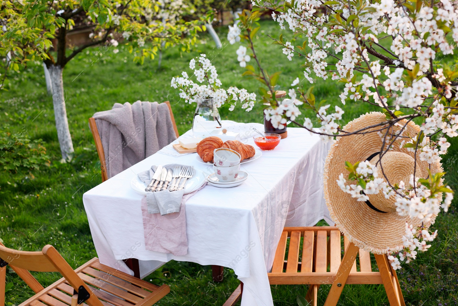 Photo of Stylish table setting with beautiful spring flowers, tea and croissants in garden