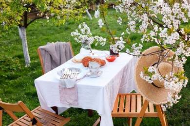 Stylish table setting with beautiful spring flowers, tea and croissants in garden