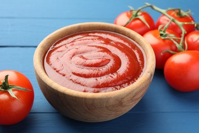 Bowl of tasty ketchup and tomatoes on blue wooden table, closeup