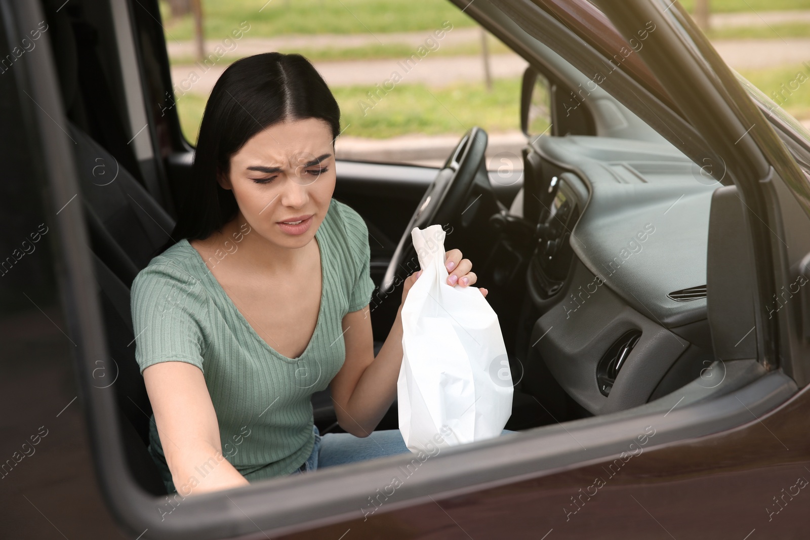 Photo of Young woman with paper bag suffering from nausea in car