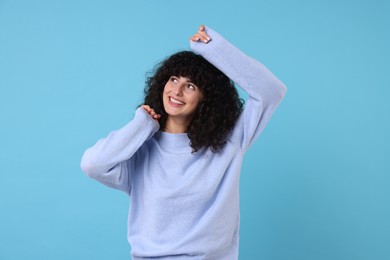 Happy young woman in stylish warm sweater on light blue background