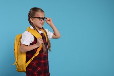 Photo of Happy schoolgirl in glasses with backpack on light blue background, space for text