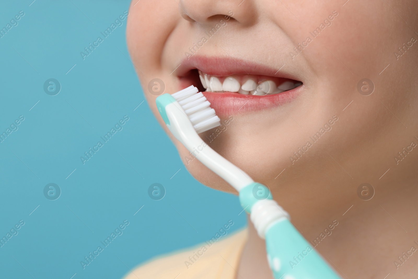 Photo of Cute little boy brushing his teeth with plastic toothbrush on light blue background, closeup. Space for text