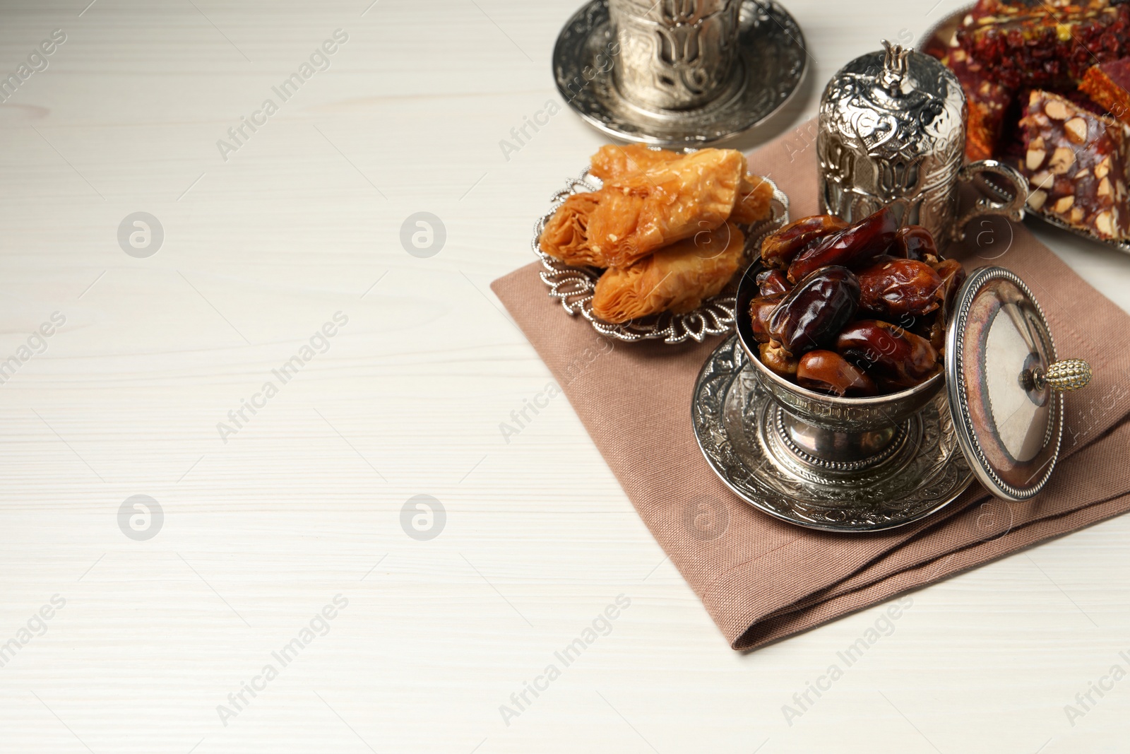 Photo of Tea, date fruits, Turkish delight and baklava dessert served in vintage tea set on white wooden table, space for text