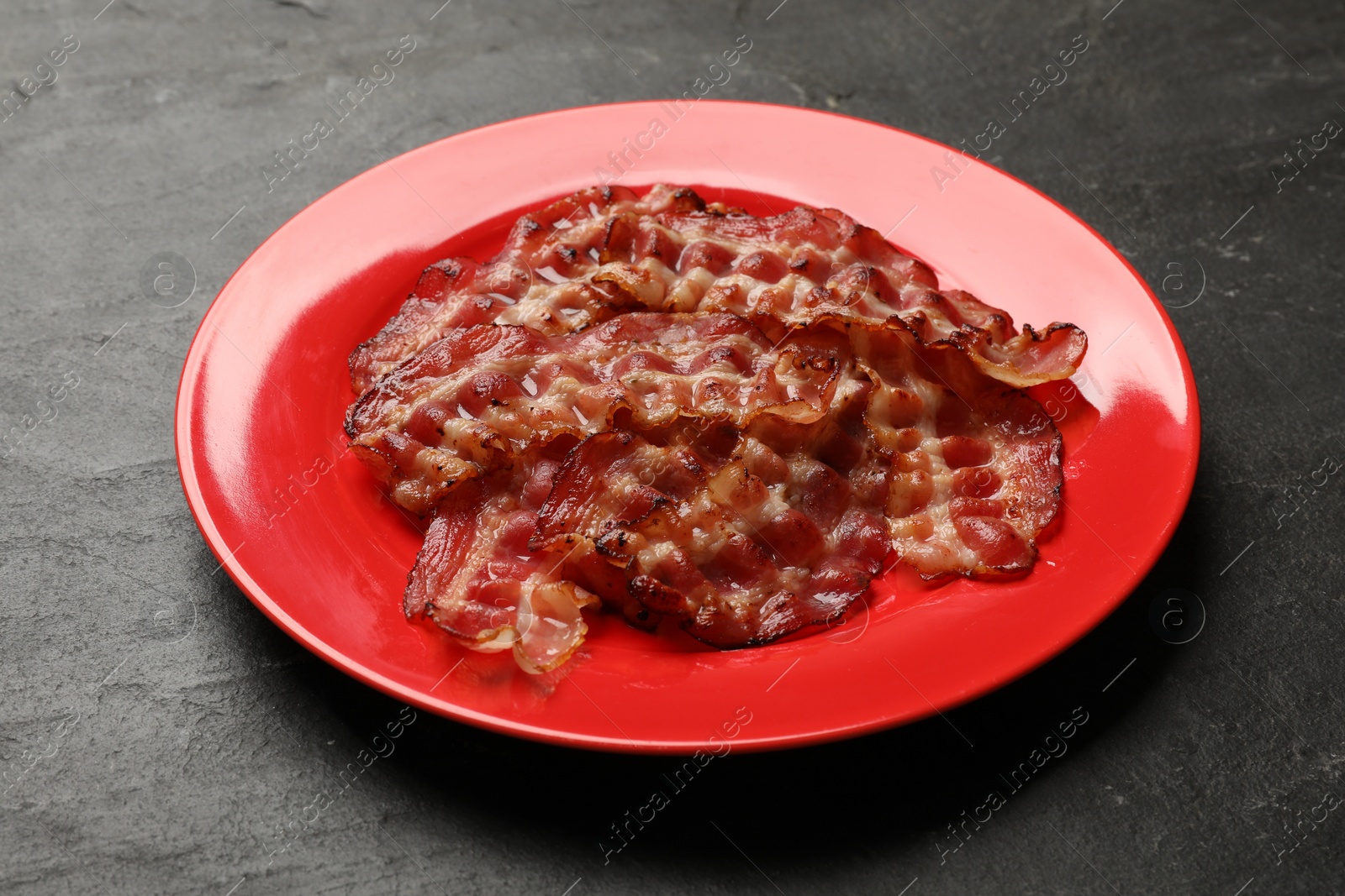 Photo of Plate with fried bacon slices on dark table, closeup