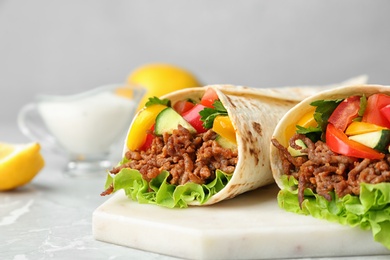 Board with delicious meat tortilla wraps on light table against grey background