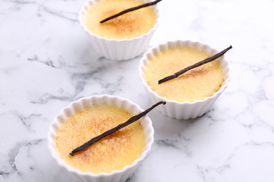 Photo of Delicious creme brulee in bowls and vanilla pods on white marble table