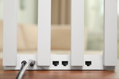 Photo of New modern Wi-Fi router on wooden table indoors, closeup