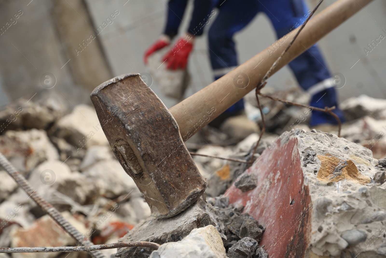 Photo of Sledgehammer on pile of broken stones. Man working outdoors, selective focus