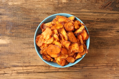 Photo of Bowl of sweet potato chips on wooden table, top view