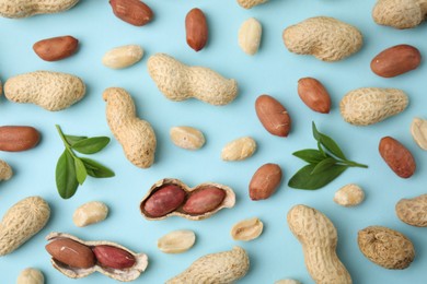 Photo of Fresh peanuts and leaves on light blue table, flat lay