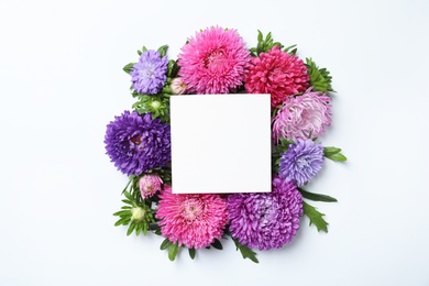 Photo of Beautiful aster flowers with sheet of paper on white background, top view. Space for text