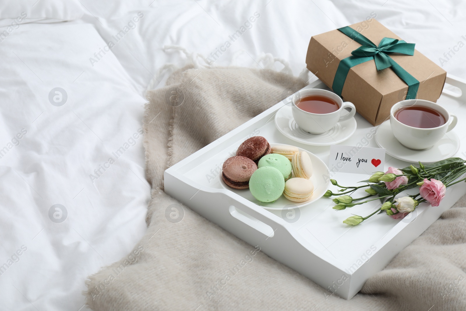 Photo of Tasty breakfast served in bed. Delicious macarons, tea, gift box, flowers and I Love You card on tray