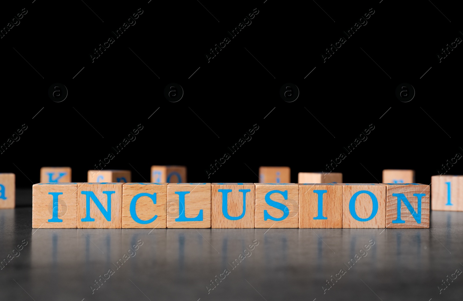 Photo of Wooden cubes with word Inclusion on dark grey table against black background. Space for text