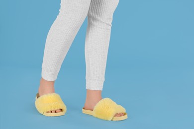 Photo of Woman in fluffy slippers on light blue background, closeup