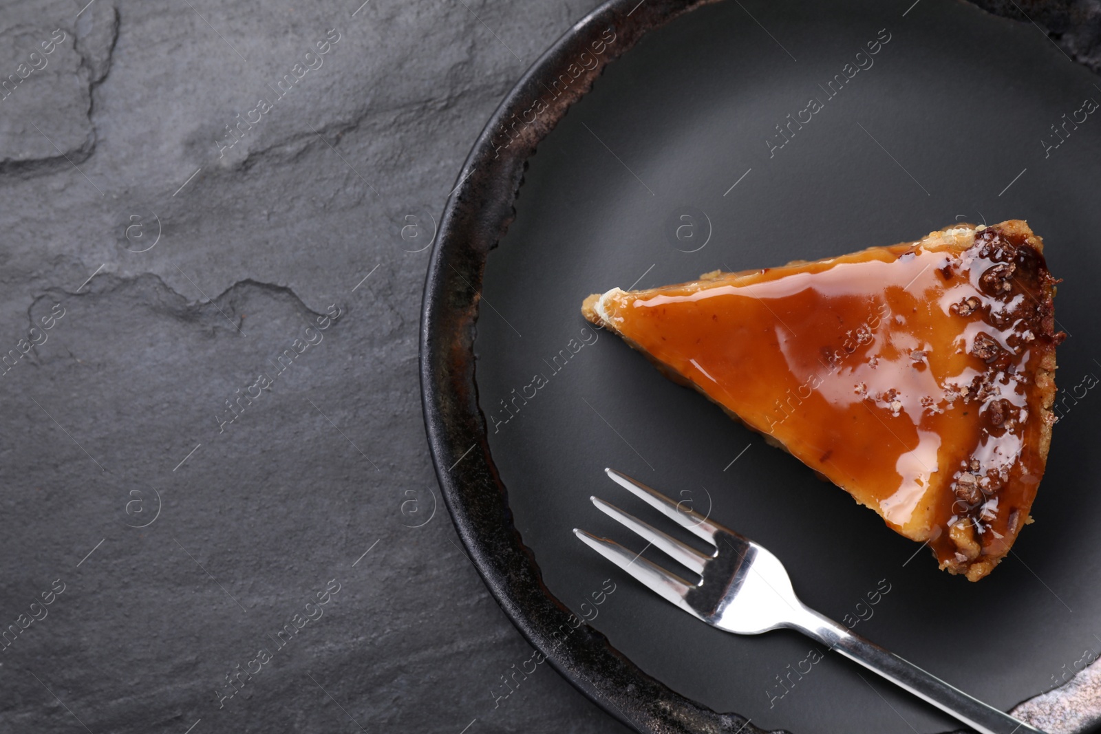 Photo of Piece of delicious cake with caramel on black table, top view