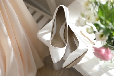 Photo of Pair of white high heel shoes, flowers and wedding dress indoors