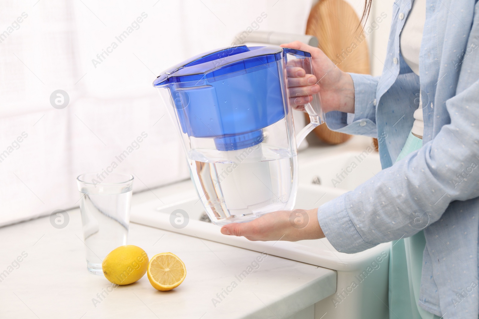 Photo of Woman with water filter jug in kitchen, closeup