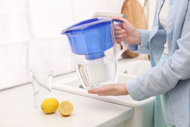 Photo of Woman with water filter jug in kitchen, closeup