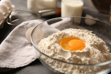 Photo of Making dough. Flour with egg yolk in bowl on grey table, closeup