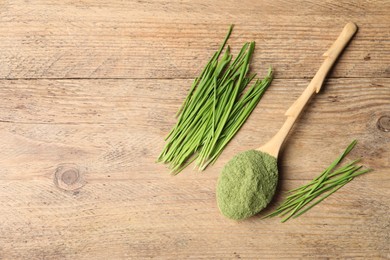 Wheat grass powder in spoon and fresh green sprouts on wooden table, flat lay. Space for text