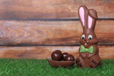 Easter celebration. Funny chocolate bunny and candies on grass against wooden background. Space for text