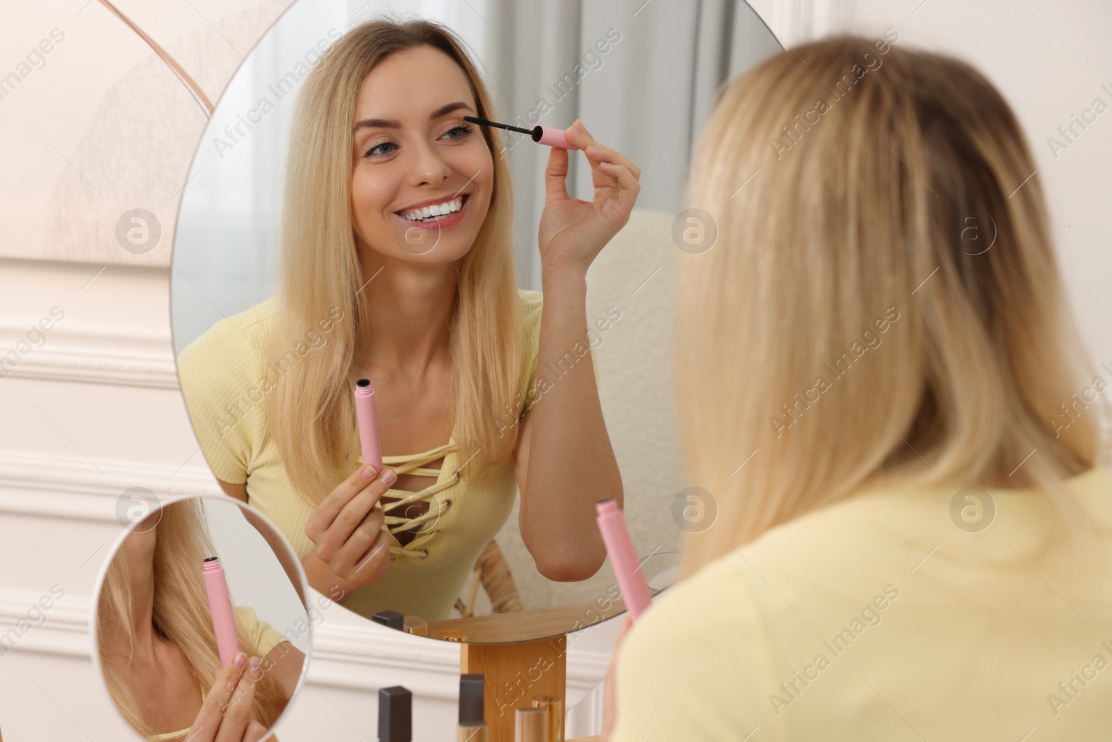 Photo of Beautiful woman applying mascara near mirror at home