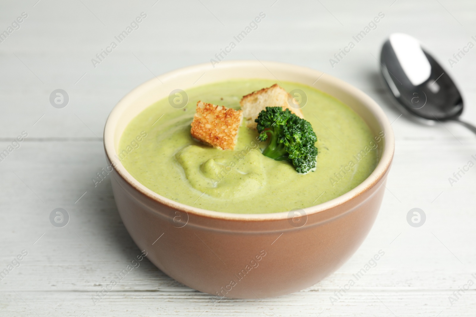 Photo of Delicious broccoli cream soup with croutons served on white wooden table