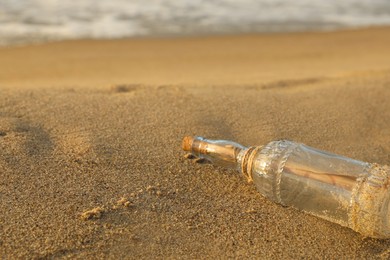 Photo of SOS message in glass bottle on sand near sea, space for text