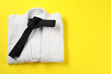 Photo of Black karate belt and white kimono on yellow background, top view. Space for text