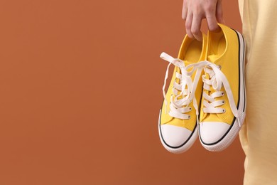 Woman with yellow classic old school sneakers on brown background, closeup. Space for text