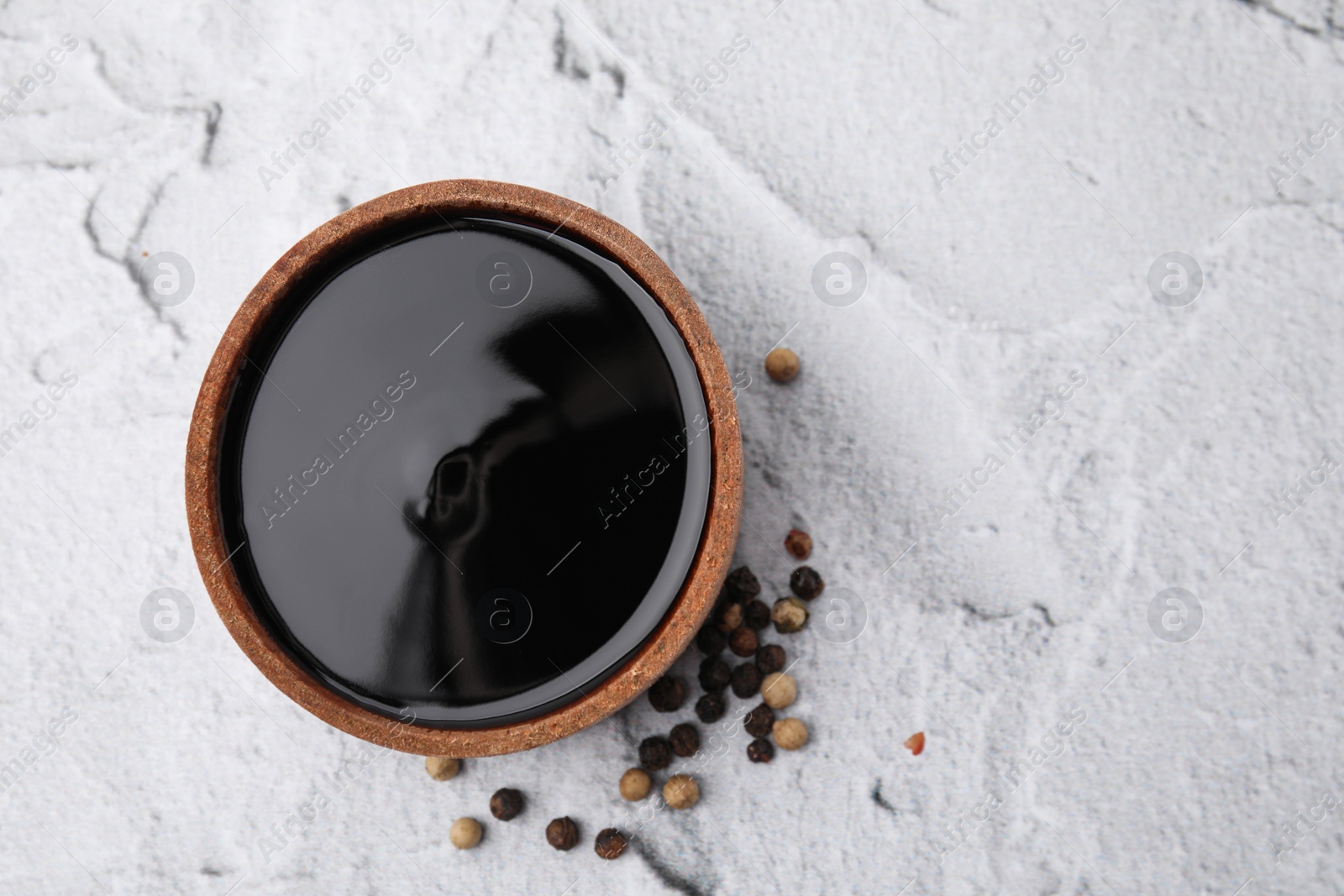 Photo of Wooden bowl with balsamic vinegar and peppercorns on white textured table, top view. Space for text