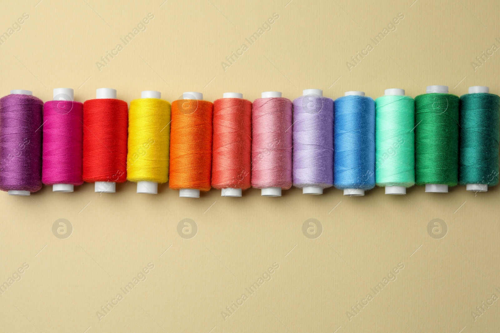 Photo of Set of colorful sewing threads on beige background, flat lay. Space for text