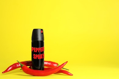 Bottle of gas pepper spray and fresh chili peppers on yellow background. Space for text