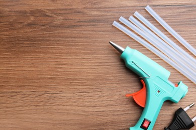 Photo of Turquoise glue gun and sticks on wooden table, flat lay. Space for text