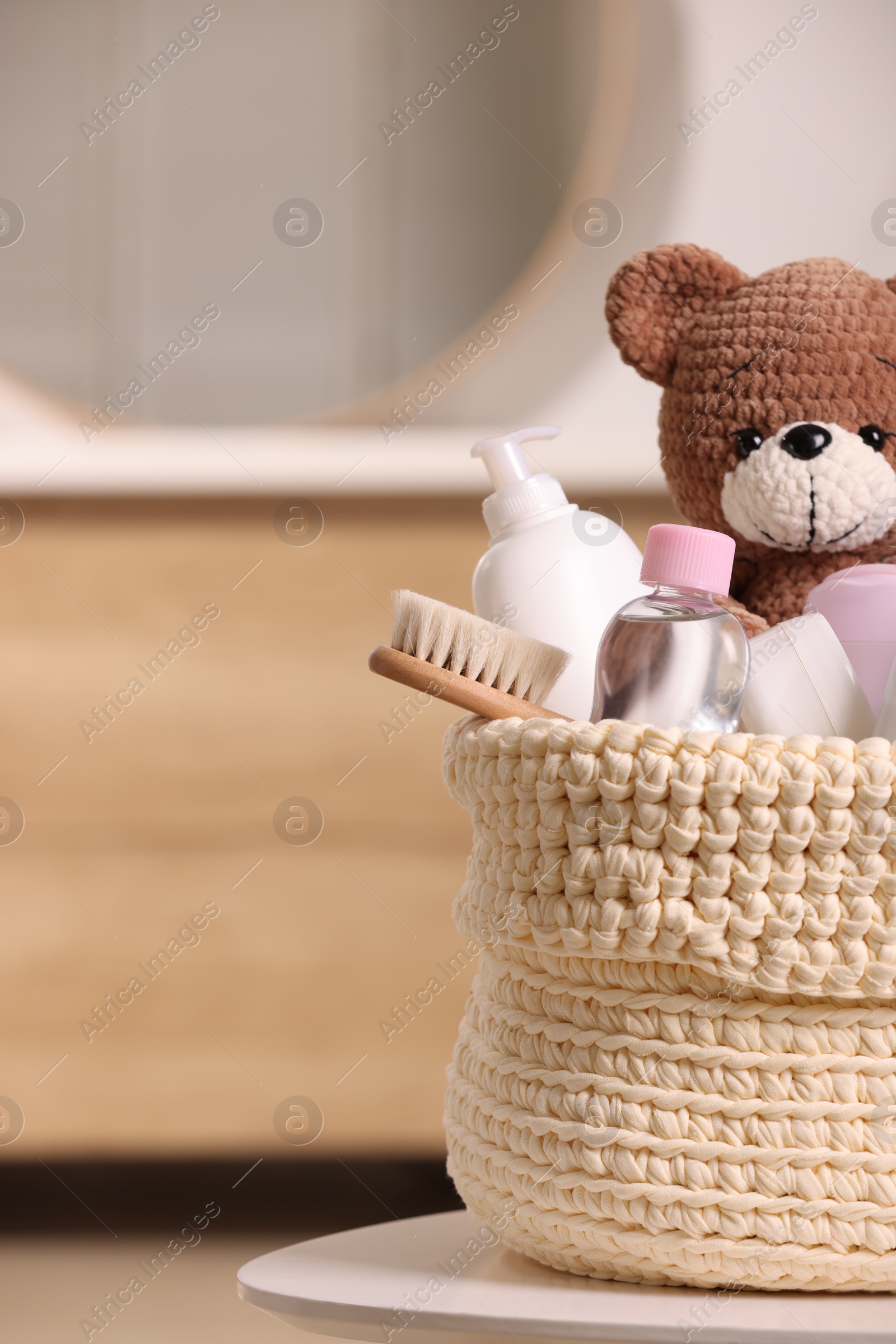 Photo of Knitted basket with baby cosmetic products, bath accessories and toy bear on white table indoors