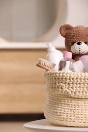 Knitted basket with baby cosmetic products, bath accessories and toy bear on white table indoors