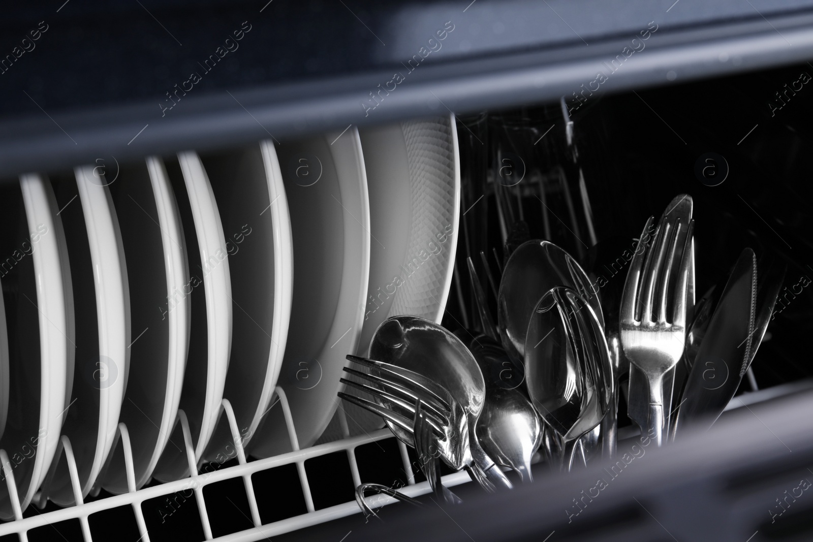 Photo of Clean plates and cutlery in dishwasher, closeup