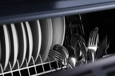 Photo of Clean plates and cutlery in dishwasher, closeup