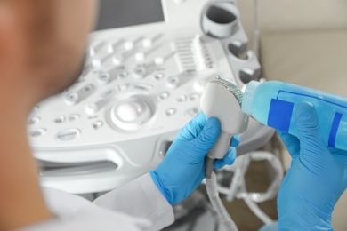 Photo of Sonographer covering ultrasound machine probe with gel in clinic, closeup