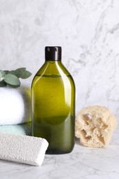 Photo of Shampoo bottle, loofah, folded towels and pumice on white marble table