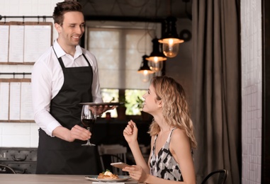 Photo of Young waiter serving wine to client in restaurant