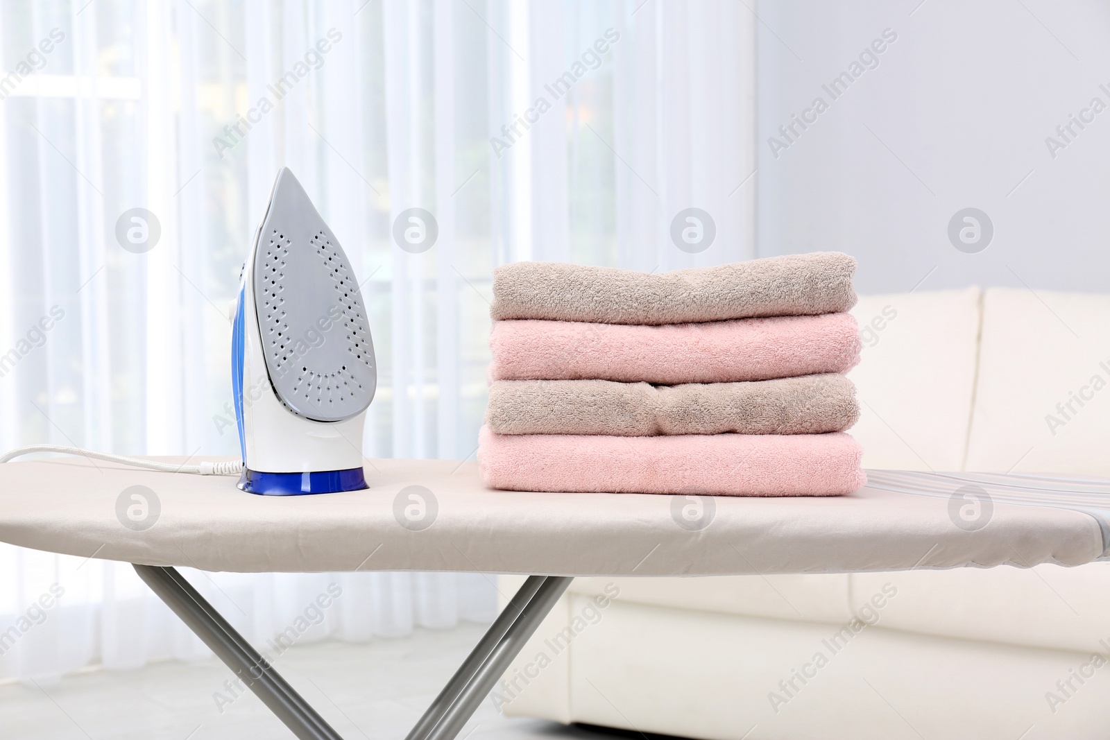 Photo of New modern iron and clean towels on board indoors. Laundry day