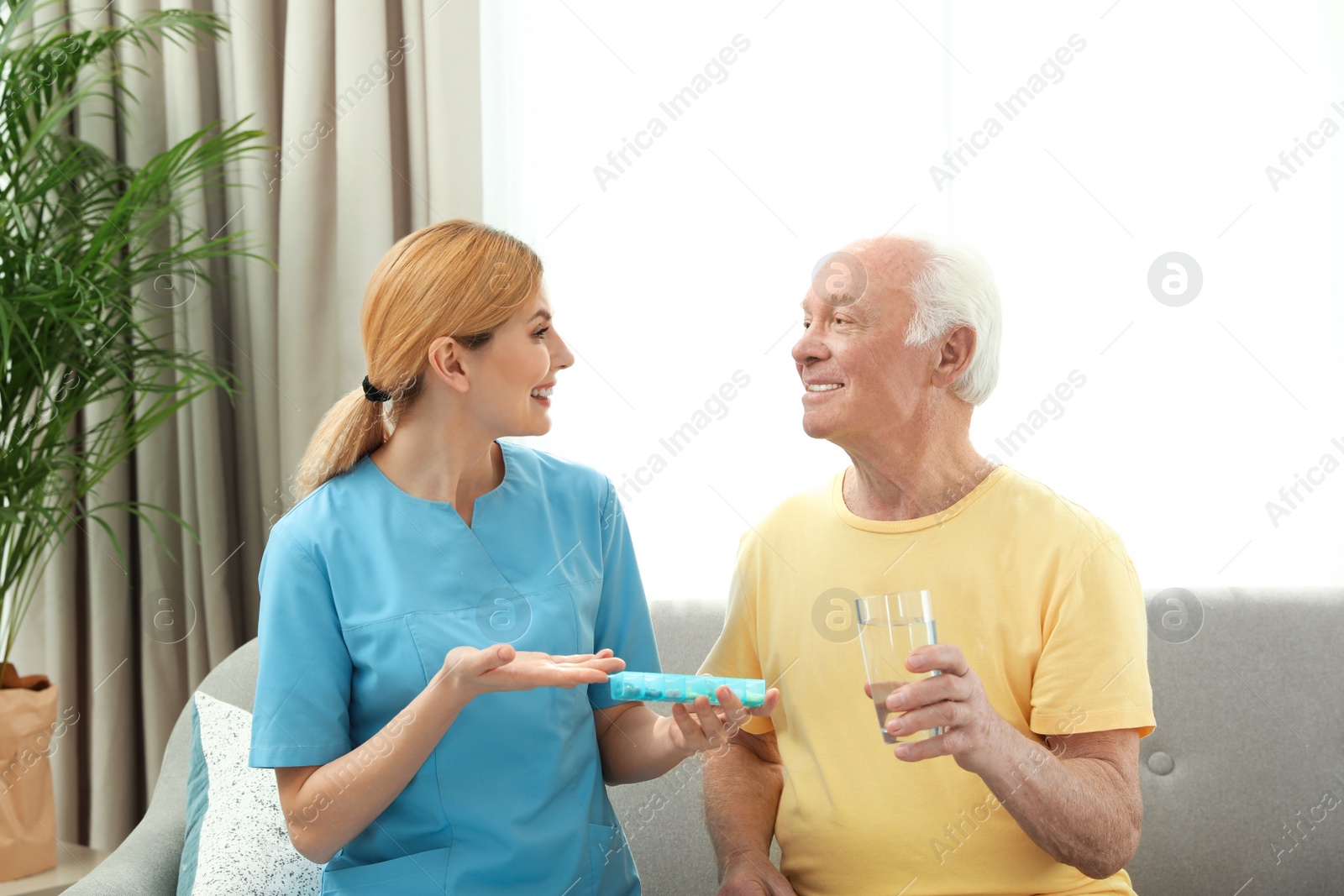 Photo of Nurse giving medication to elderly man indoors. Assisting senior people